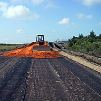 Planierraupe verteilt Sand über einem verlegten Basetrac Grid Geogitter zur Tragschichtbewehrung auf einer Baustelle