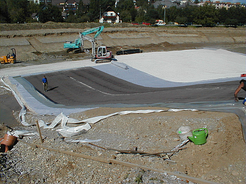 Geosynthetische Tondichtungsbahnen werden per Bagger verlegt