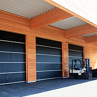 Black Tectura Stabitore on a wooden warehouse. A forklift truck and cars are parked in front of it