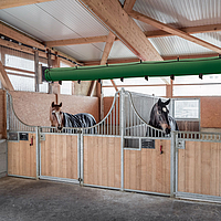 Lubratec Tube Cool an der Decke eines Pferdestalls und oberhalb von zwei Pferdeboxen mit Pferden