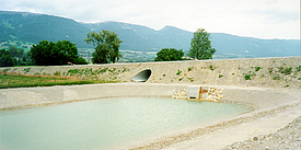 Mit Betonmatten und Schüttsteindeckwerk abgedichtetes und mit Wasser gefülltes Regenrückhaltebecken