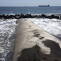 Eingebauter geotextiler Wellenbrecher im Meer im Hintergrund Wasserbausteine gegen die die Wellen schlagen