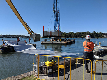 Bagger und Kran lassen Aktivkohle Geokomposit ins Wasser