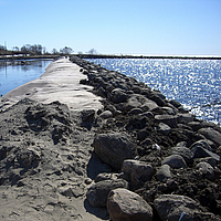 Damm aus Geokunststoffen, verkleidet mit Steinen und Sand